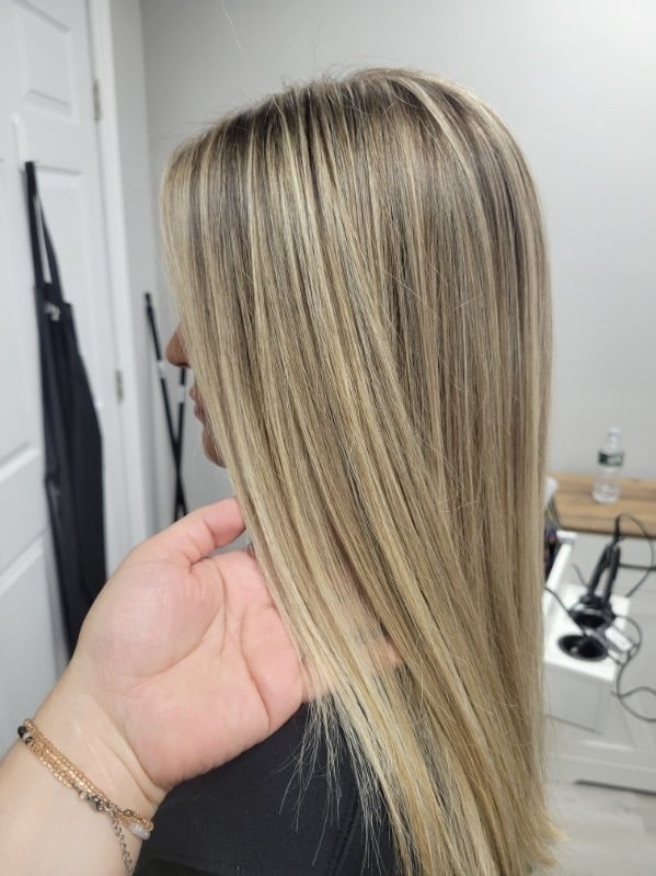 Person displaying long, straight, blonde hair with subtle highlights in an indoor salon setting
