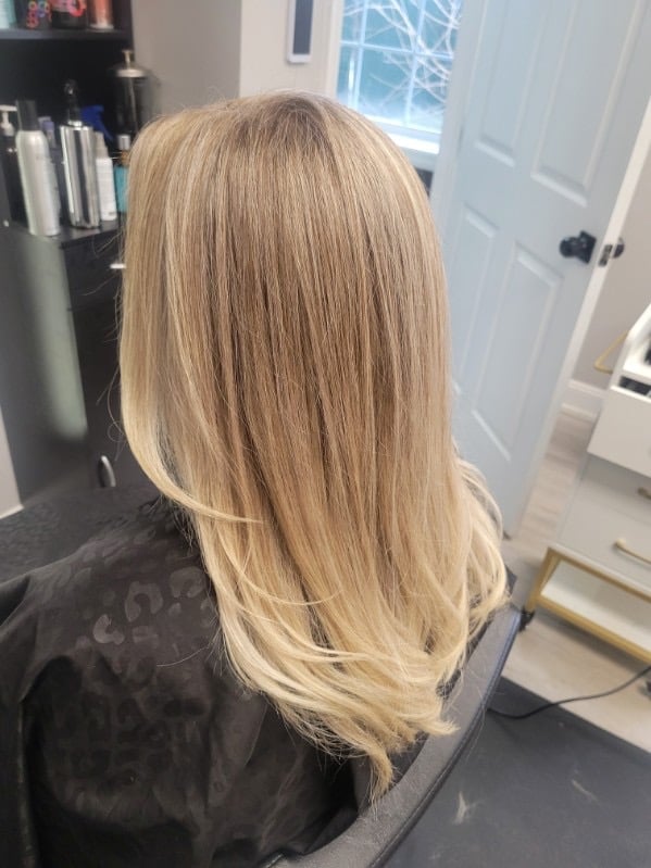 Back view of a woman with long, straight blonde hair in an indoor setting with white doors and shelving visible