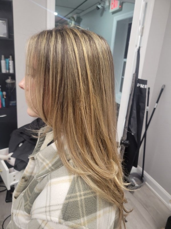 Woman with long, straight caramel-highlighted brown hair shown from behind in a salon setting