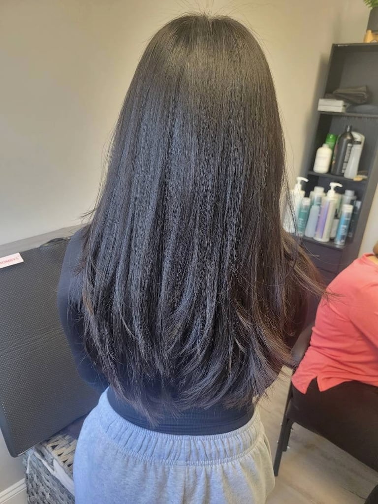 Back view of woman with long straight dark hair in a salon setting with hair care products on shelves